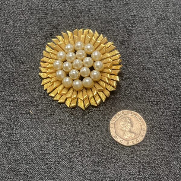Close-up of vintage sunburst brooch with pearls on dark fabric.