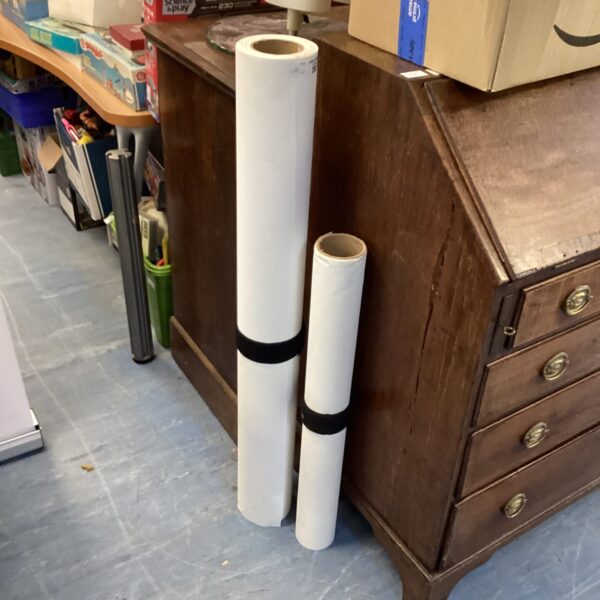 Two rolls of artist canvas displayed near a wooden cabinet.