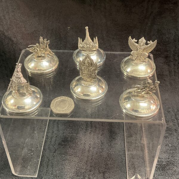 Set of six ornate Thai sterling silver place setting holders on display.