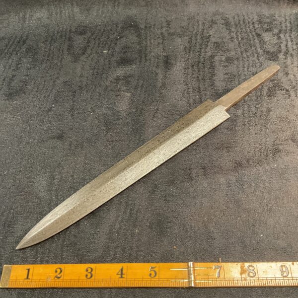 Unfinished Damascus steel knife blade with visible forging patterns.
