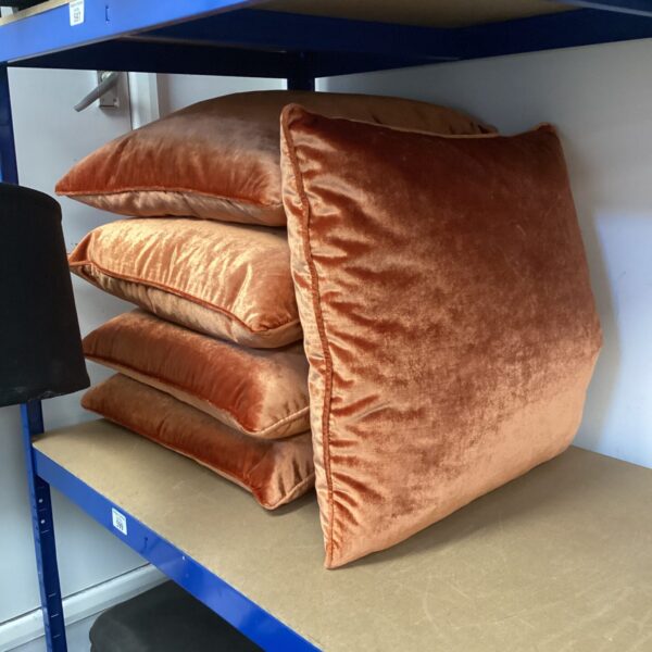Five metallic orange velvet cushions stacked neatly.