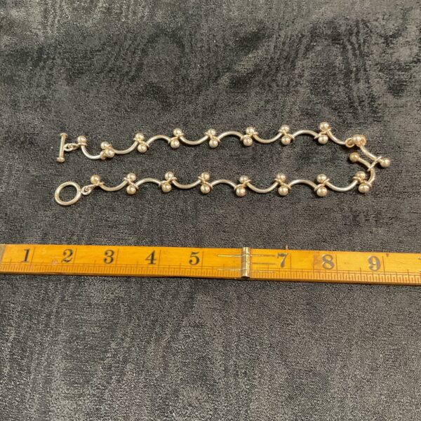Close-up of a chunky silver T bar necklace on a neutral background.