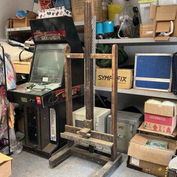Large vintage wooden artist easel in a cluttered room.