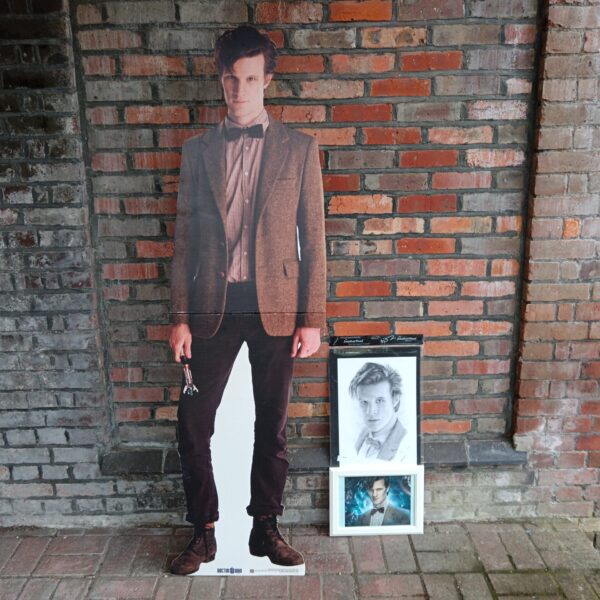 Life-size Matt Smith Doctor Who cardboard cutout against brick wall.