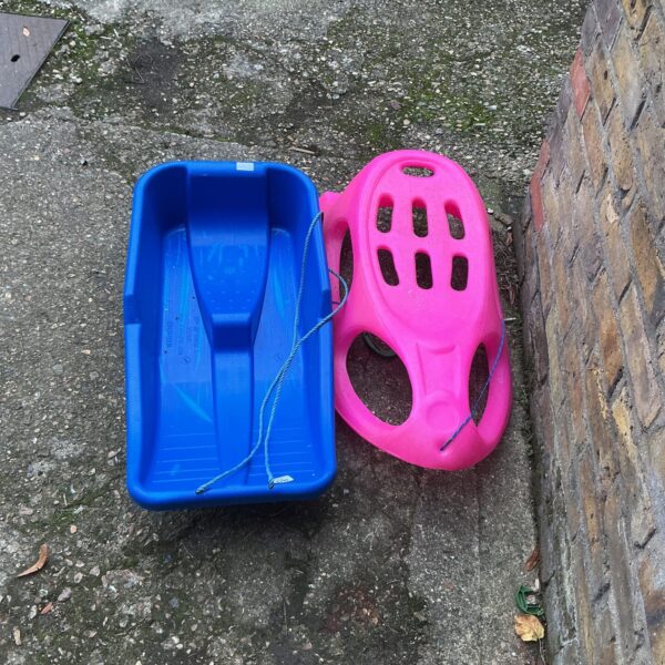 Two colourful plastic toboggans for winter snow fun.