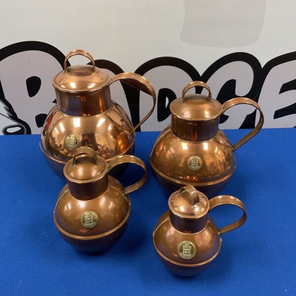 Set of four graduated Guernsey copper milk cans for farmhouse decor.