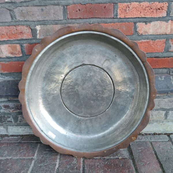 Large hammered copper bowl with scalloped rim against brick wall.