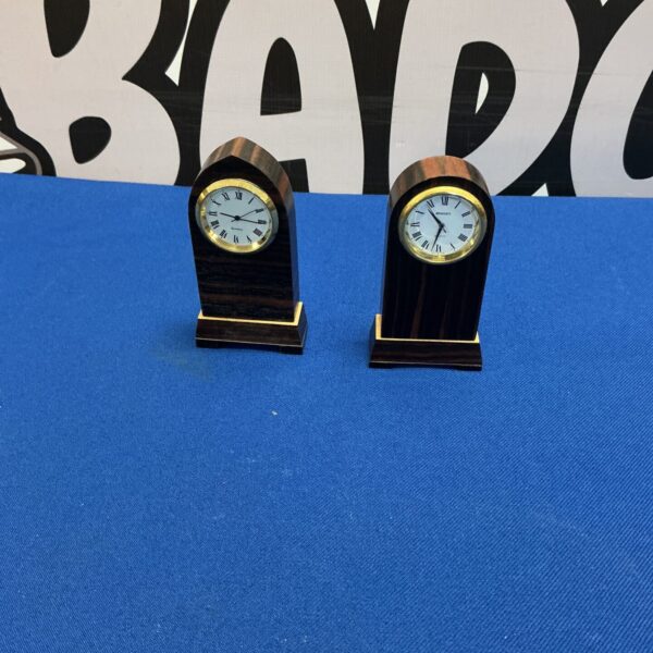 Pair of vintage miniature mantle clocks on a dark surface.