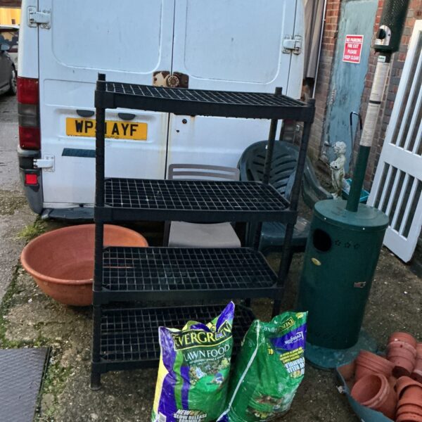Black plastic shed shelving unit in a garden setting.