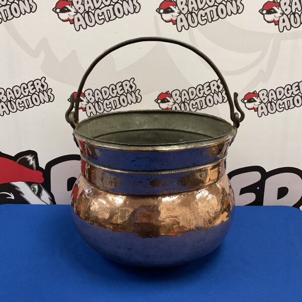 Large antique copper cauldron with handles, showing age and patina.