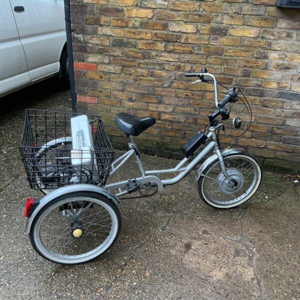 Silver electric tricycle with basket, side view.