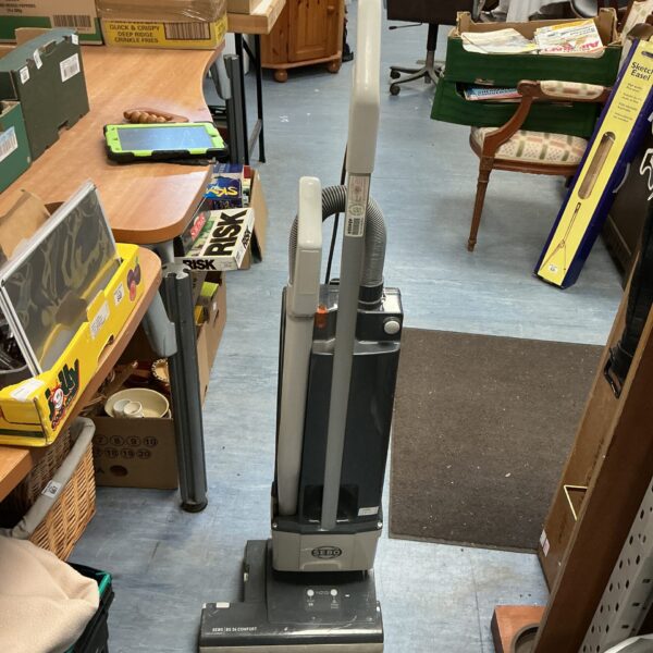 Upright Sebo vacuum cleaner in a cluttered room.