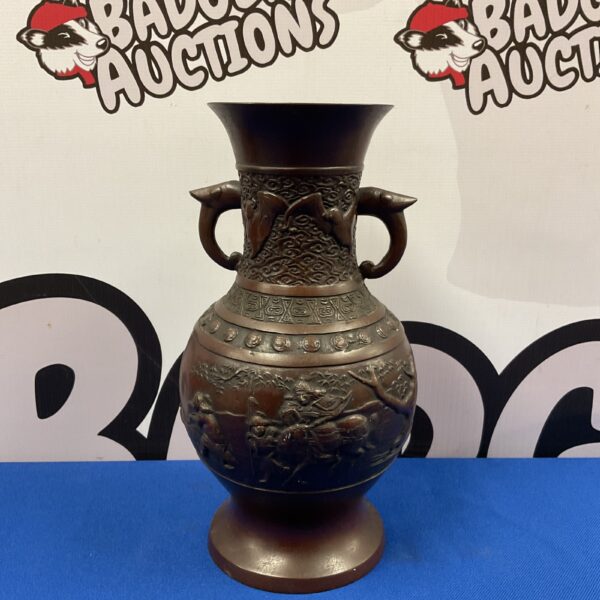 Antique Chinese bronze vase with warrior carvings on a blue background.