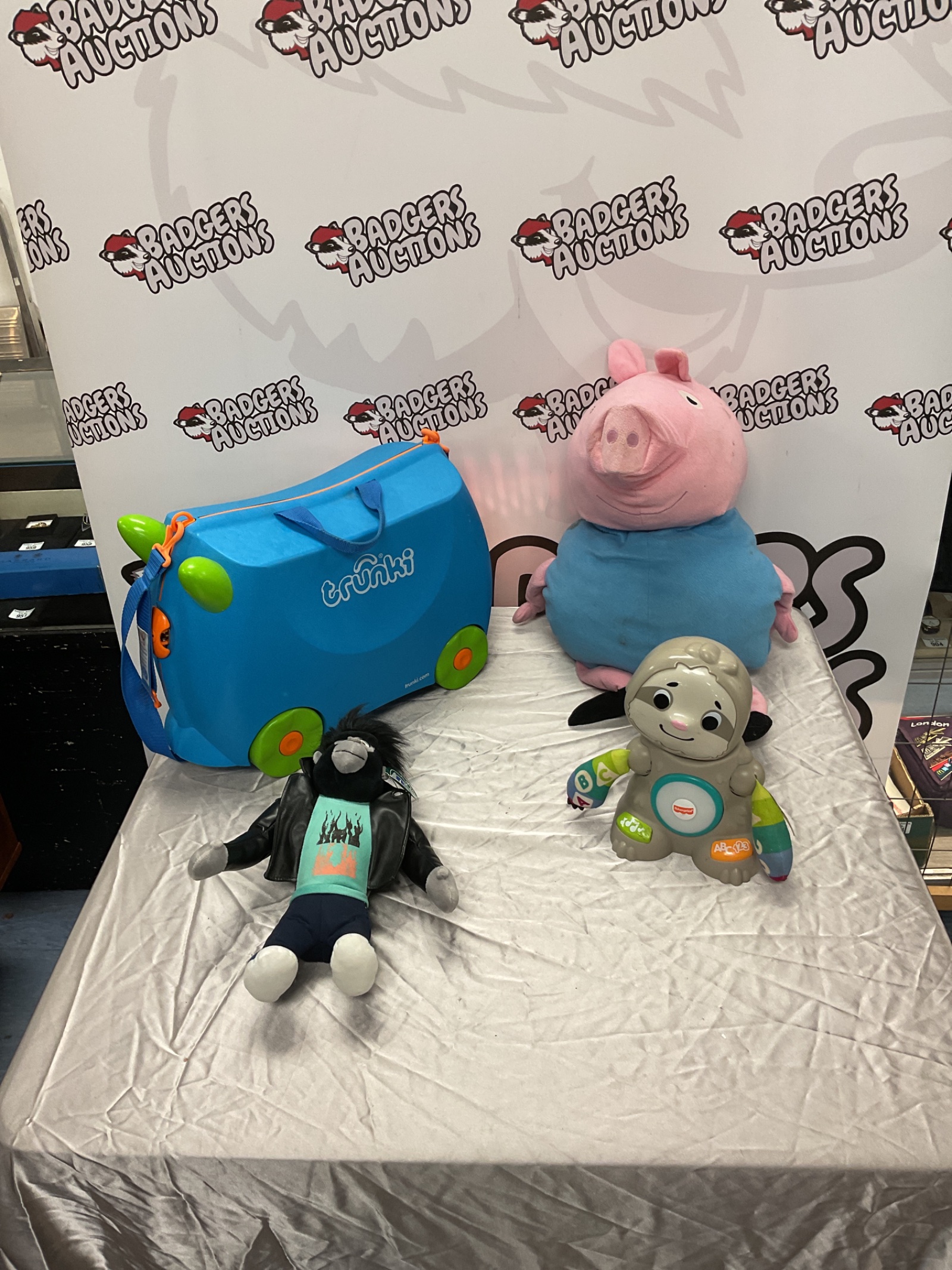 376 Trunki kids case, plush George from Peppa Pig, Johnny from Sing 2, and Fisher Price sloth toy