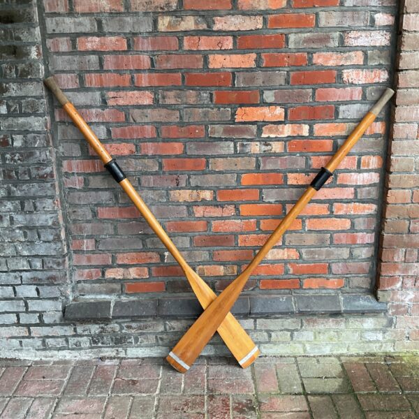 Vintage Norwall boat oars displayed against a brick wall.