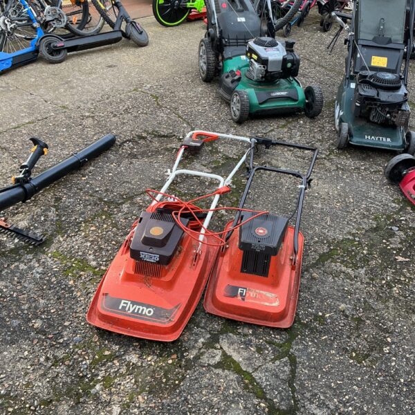 Two used Flymo electric lawnmowers in a garden setting.