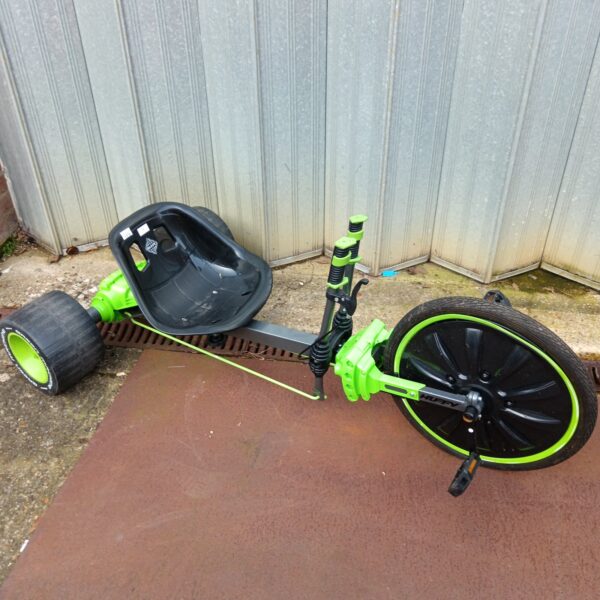 Green Machine trike with buckled front wheel, outdoor ride on toy.