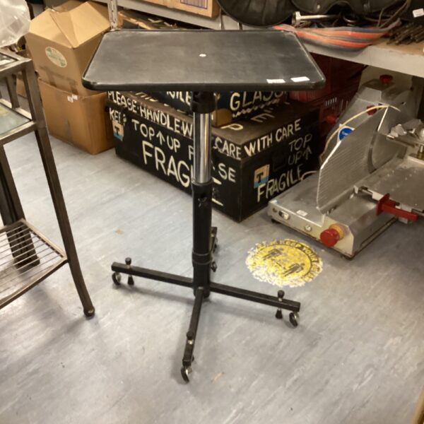 Black mobile projector table with adjustable height and tilting surface.
